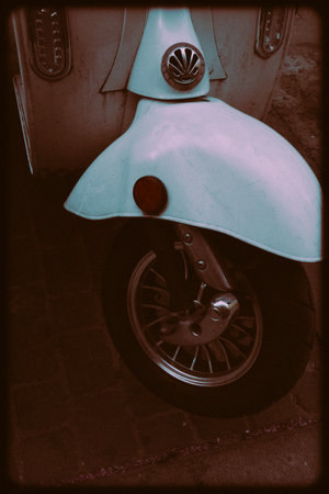 Vintage retro two wheeler blue scooter upright photo with black frame. Eco-friendly urban transportation for traveling. Dark key motorbike outdoors.の写真素材
