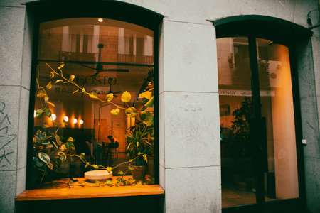 Madrid, Spain. May 1, 2023 Cafe, coffee shop facade, entrance. Panoramic windows with yellow electric lighting indoors in the evening street at a duskのeditorial素材