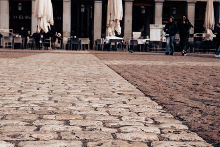 Madrid, Spain. 1 March 2024 Cafe terrace with tables, umbrellas on old city street Antique stone...