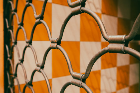 Cage metal net arranged in a pattern on yellow white tile wall background. Fence mesh. Metallic lattice in a form of rhombuses. Security concept.の写真素材
