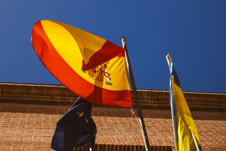 May 1, 2024 Yellow-red flag of Spain develops against blue sky, a flag of the European Union, a flag...