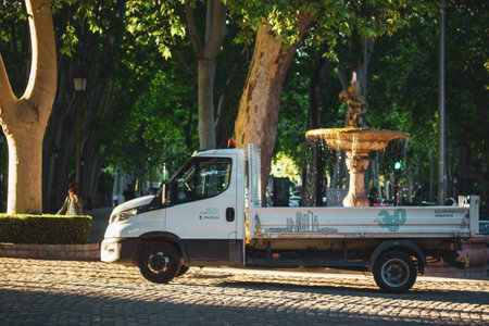 Madrid, Spain. 1 May 2024 Open box truck in city park. Compact car, white van in front of an old fountain on the old city street. Open body truck.のeditorial素材