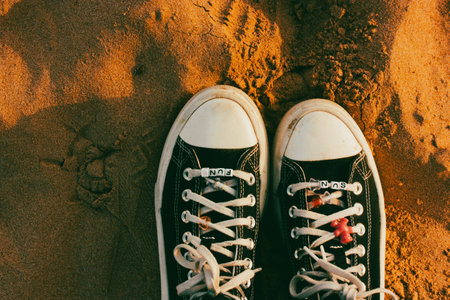Old sneakers on female feet top view. Footwear foot fashion. Shoes on a yellow sand. Nostalgia for...