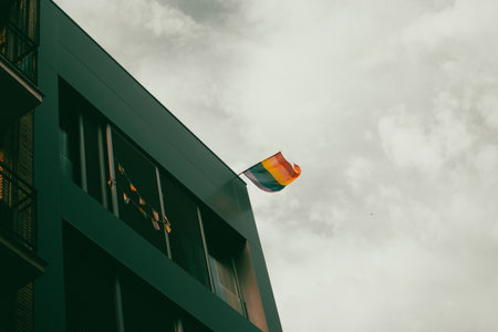 A multicolored LGBT flag on a modern building corner against sky. Diversity, gay minority, pride month symbol. Lesbians, gays community. Pride month.の写真素材