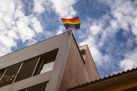 A multicolored LGBT flag on a modern building corner against sky. Diversity, gay minority, pride month symbol. Lesbians, gays community. Pride month.の写真素材