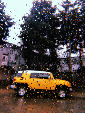 Blurred bright yellow SUV car parked outside. Vertical wet window texture with rain drops. urban city street in autumn fall season day. Autumn trip.の写真素材