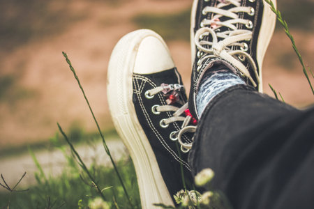 A young girl in black and white sneakers relaxing sitting on a green lawn in summer. Rest in nature....