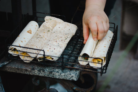 Cooking in the open air. A woman cooks pita tortillas on an outdoor barbecue fire. Vegetarian BBQ food preparation. Hand rolling vegetables wraps.の写真素材