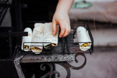 Cooking in the open air. A woman cooks pita tortillas on an outdoor barbecue fire. Vegetarian BBQ food preparation. Hand rolling vegetables wraps.の写真素材