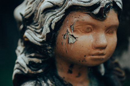 Worn stone angel. Vintage female figurine with shabby paint on her face. Monument in a cemetery. Old statue close up. Sadness, longing, depression.の写真素材