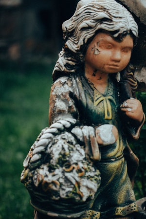 Worn stone angel. Vintage female figurine with shabby paint on her face. Monument in a cemetery. Old statue close up. Sadness, longing, depression.の写真素材