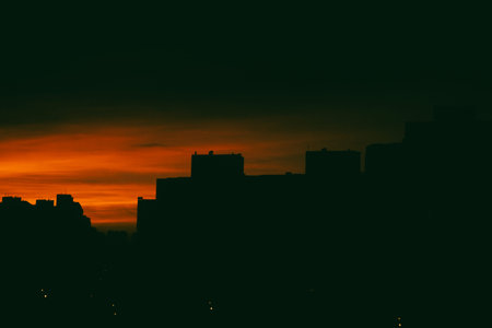 Abstract cityscape at sunset with bright orange sky and silhouettes of high-rise buildings against...