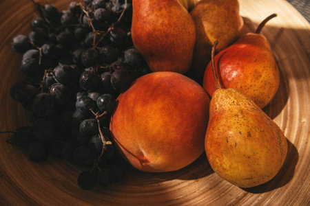 Ripe sweet seasonal fruits - peaches, pears, blue grapes in a wooden round bowl, basket close-up. Fresh rape organic summer harvest from an orchard.の写真素材