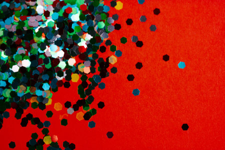 Multicolored shiny round confetti scattered on a red background. Festive decor. Wallpaper with space...