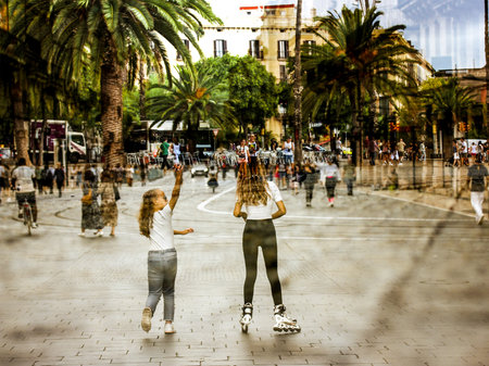 Two girls roller skating outside on a sunny day under palm trees. Travel, summer vacation. The sisters on city street. Happy childhood. Summertime.の写真素材