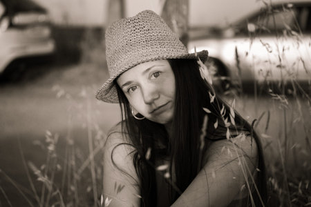 A beautiful cute young woman in a straw hat resting on the lawn among grasses in summer. Sepia female portrait. Summertime vacation trip, journey.の写真素材