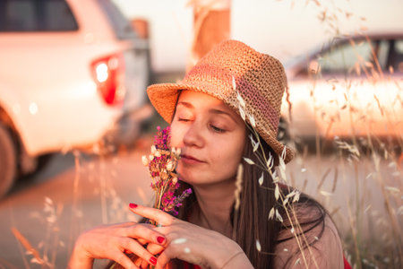 A beautiful young woman in a straw hat with a bouquet of wildflowers resting in the nature in summer. Cinematic female portrait. Summertime vacation.の写真素材