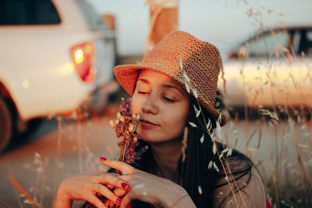 A beautiful young woman in a straw hat with a bouquet of wildflowers resting in the nature in summer. Cinematic female portrait. Summertime vacation.の写真素材