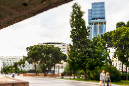 Abstract city street with glass facade skyscraper, green trees and people walking on the street during daytime. Urban lifestyle. Cityscape nature.の写真素材
