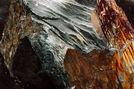 Big stone with rough corners. A gray brown rock with sharp edges and textured surface on a black sand. Natural stones rocksの写真素材