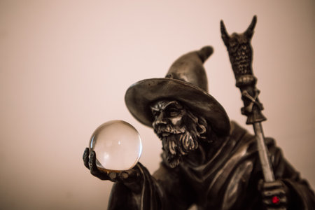Dark wizard looking in a crystal magic ball in his hand. Fortune teller looks into the future. Halloween concept. Magician wearing a hat with red ringの写真素材