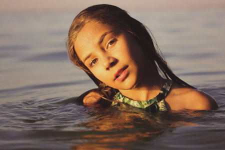 A young girl enjoys a swim in the ocean, captured during the golden hour, showing her peaceful...