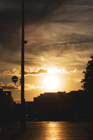 Buildings silhouetted against a sunset, a street lamp stands tall, casting shadows across the urban landscape. The sun provides a beautiful warm glow.の写真素材