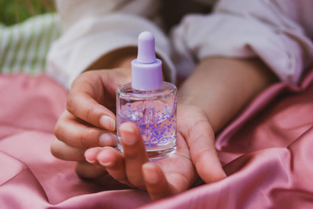 Cosmetic dropper bottles rest delicately in open female hands on a soft pink satin fabric The colors...
