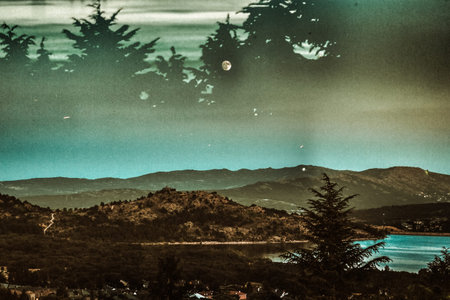 A serene landscape showcases rolling hills and a tranquil lake under moody sky adding a touch of...