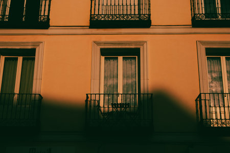 A warm toned building facade with balconies A table and chairs sit on one balcony behind a wrought-iron railing. A setting is lit by a warm soft lightの写真素材