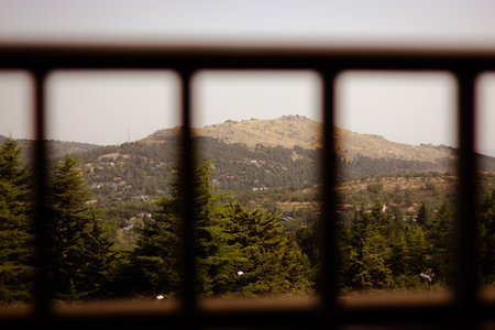 Looking through metal frame at a mountain A scenic view of a mountains is framed by a dark square metal railing. Lush green trees fill the foreground.の写真素材