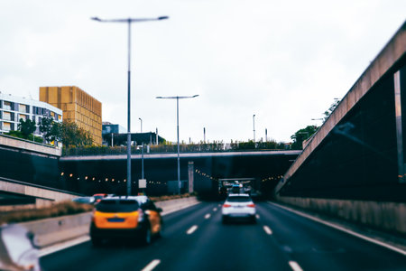 Vehicles drive through a tunnel on a multi-lane highway, buildings lining the sides, cloudy skies overhead. The perspective is from the driver's seat.の写真素材