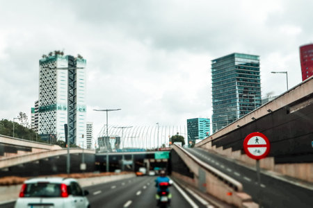 Vehicles drive through a tunnel on a multi-lane highway, buildings lining the sides, cloudy skies...