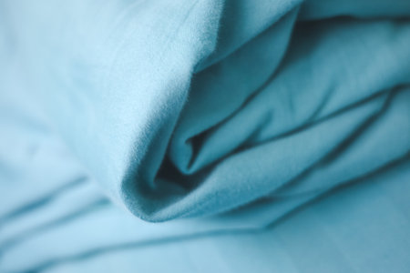 A close-up shot of teal-colored fabric, with soft folds and textures. The smooth material is elegantly draped, highlighting subtle shadows and form.の写真素材