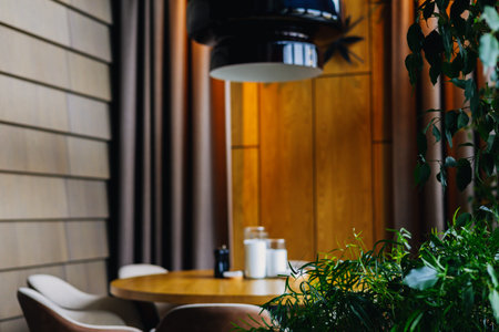 An inviting restaurant interior with a round wooden table, stylish chairs decorative elements, complemented by lush green plants and a modern lightingの写真素材