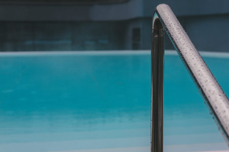 A close-up shot captures the water droplets on a polished handrail next to the clear pool water. The...