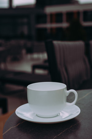 A pristine white cup and saucer, elegantly placed, creating a calm and inviting atmosphere. A white cup and saucer sit on a dark table, a peaceful scene suggestive of a relaxed break or tranquil moment.の写真素材