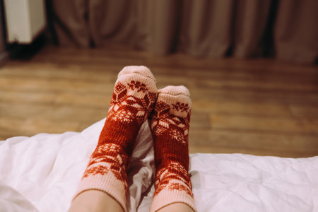 Female feet wearing festive patterned socks, relaxing on bed indoors. Cozy feet resting on sofa, warm, patterned winter socks. Comfort relaxing momentの写真素材