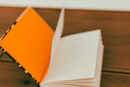 A close-up shot of an open notebook with an orange cover and blank pages on a wooden surface. A book is seen with blank pages ready for notes. Plannerの写真素材