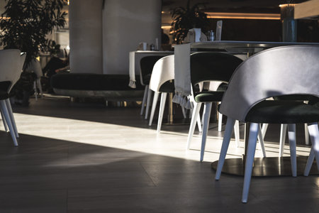 Modern restaurant interior is seen with chairs and tables illuminated by sunlight, creating a...