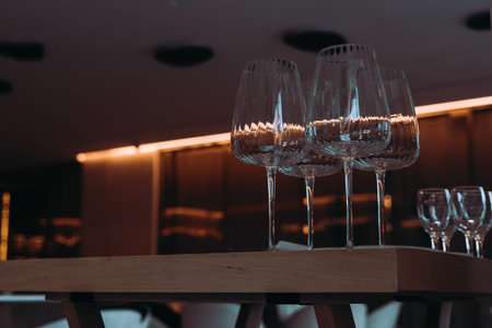 Crystal wine glasses, arranged on a wooden table with warm lighting. Elegant wine glasses sit atop a...