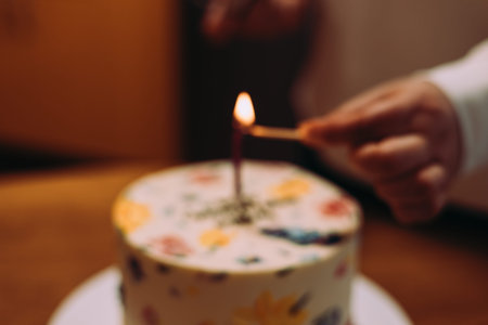 A blurred image of a hand lighting a candle on decorated birthday cake. A colorful, floral-decorated cake, ready for a celebration. Perfect for birthdays or other special occasions. Congratulations.の写真素材