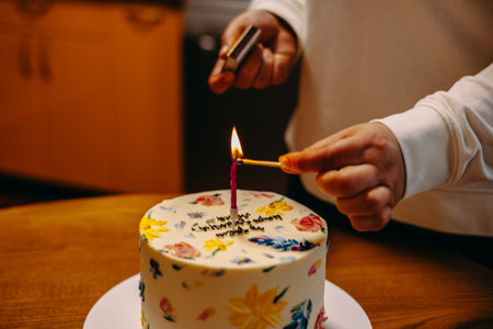 A hand is lighting a candle on a cake decorated with lovely floral designs, ready to enjoy. A hand lights a candle on a beautifully birthday cake. A festive cake is adorned with floral decorations.の写真素材