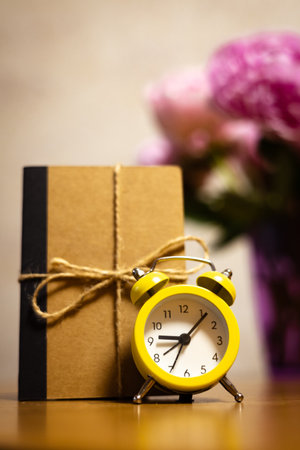Beautiful pink peonies in a purple vase with a vintage alarm clock and a notebook. A delicate bouquet of pink spring flowers on a wooden table at homeの写真素材