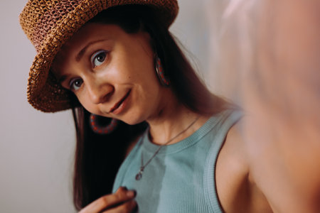 A woman in a straw hat smiles, creating an inviting portrait with soft lighting. A woman smiles while wearing a hat, a necklace, and hoop earrings, creating a warm, inviting portrait in natural light.の写真素材