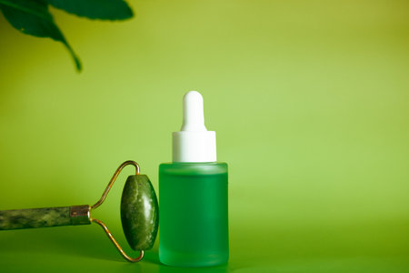 A jade facial roller and skincare serum bottle, self-care routine. Skincare serum bottle sit against a gradient green background spa-like aAesthetic.の写真素材