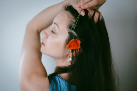 A young woman with dark hair with a red poppy flower, in a tranquil moment. A girl with long hair with eyes closed, in a moment of quiet contemplationの写真素材