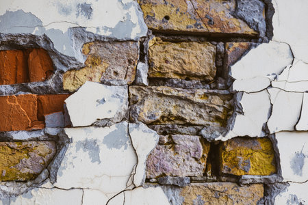 Detailed view of an old brick wall with cracked paint showing signs of aging and decay. Close-up of a weathered brick wall with peeling paint, revealing the aged texture of the building material.の写真素材