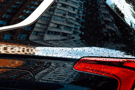 Close-up of a black car's tail light, glistening with raindrops, creating a striking visual. A close-up shot of the sleek tail light on a wet dark car. Raindrops glisten on the surface, a moody scene.の写真素材