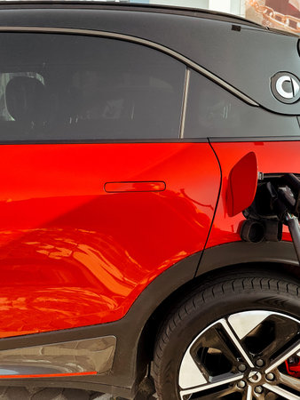 A red electric car plugged into a charging station, ready to power up. A red modern electric car is...